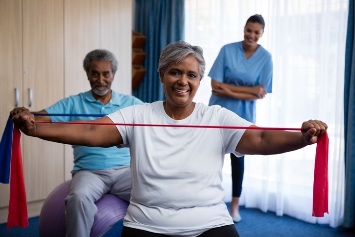 Two senior residents exercise with resistance bands while a nurse assists during outpatient therapy at Alpine Skilled Nursing and Rehabilitation in Ruston, LA.