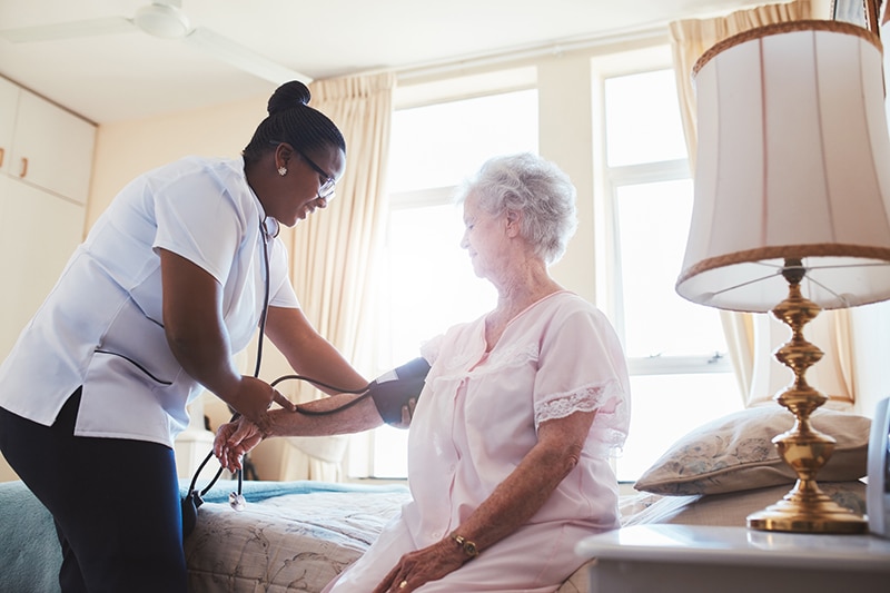 A nurse checks a senior resident's blood pressure in a comfortable, homelike private room at Alpine Skilled Nursing and Rehabilitation in Ruston, LA.