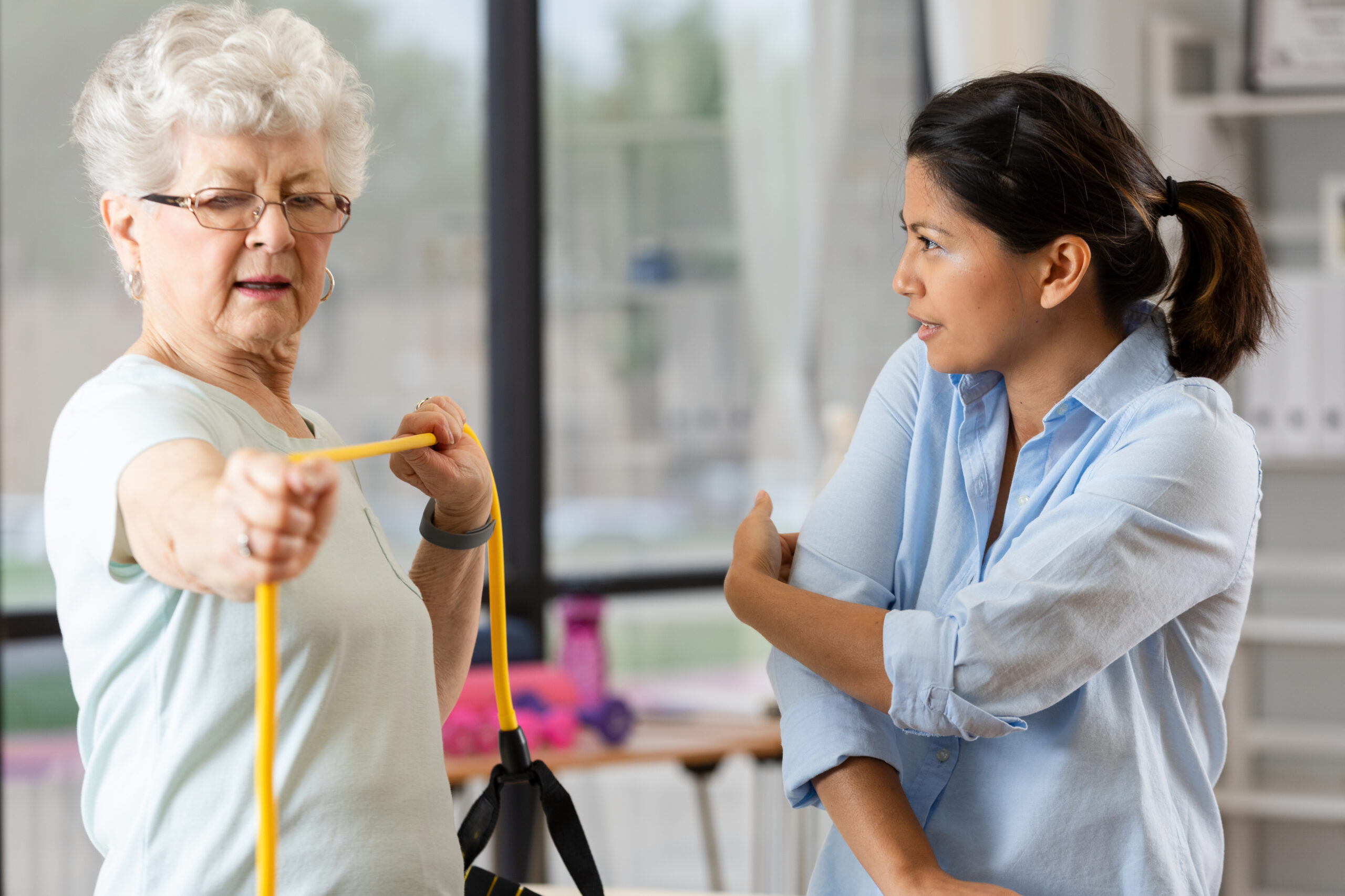 Physical therapist assists senior woman with resistance band exercise for arm strength