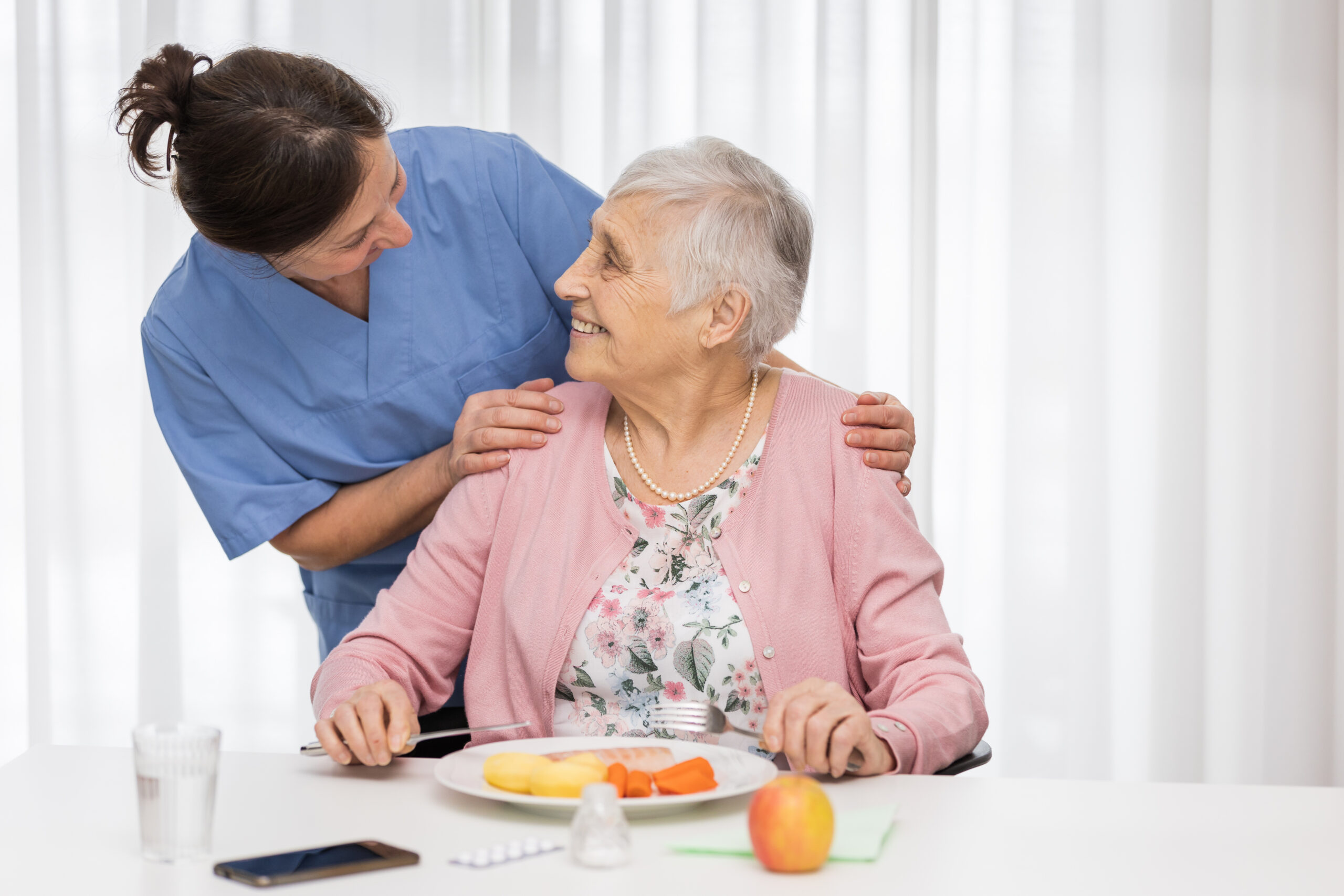 Home caregiver with senior woman, serving a meal